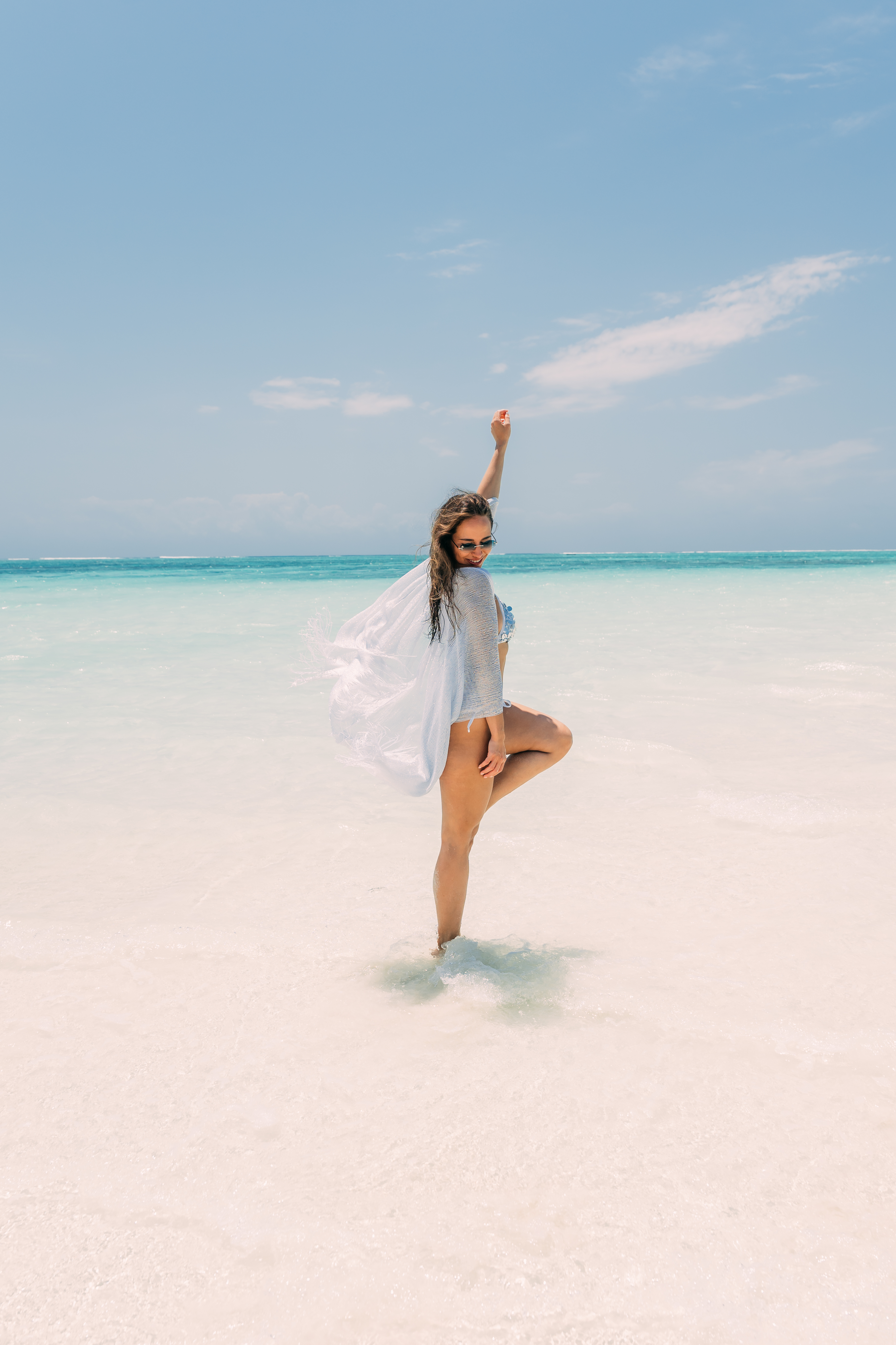 Woman in light blue bikini standing in shallow turquoise water at Nungwi beach Zanzibar with clear sky