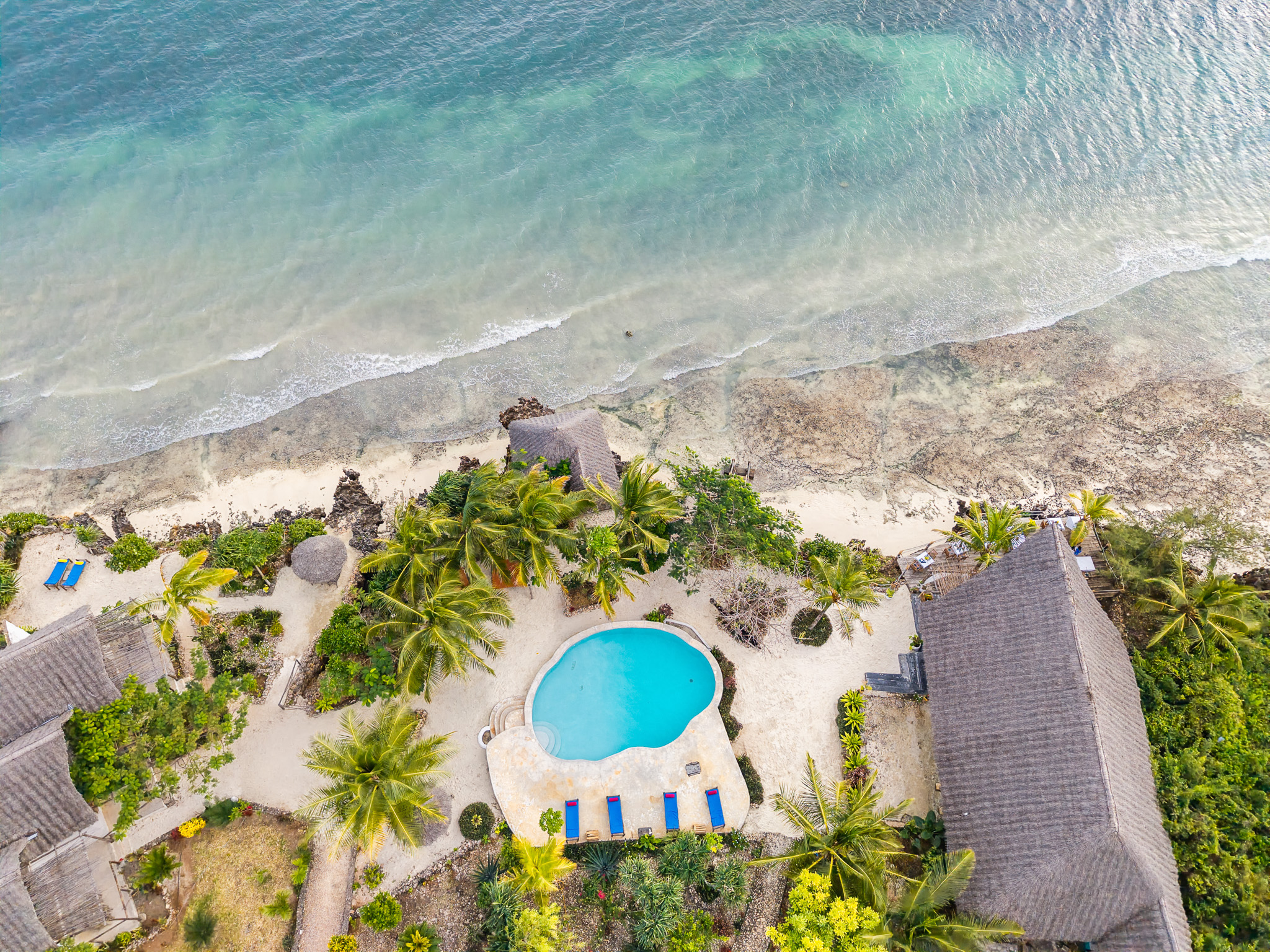 Aerial drone view of hotel pool area with lounge chairs and beach in Zanzibar