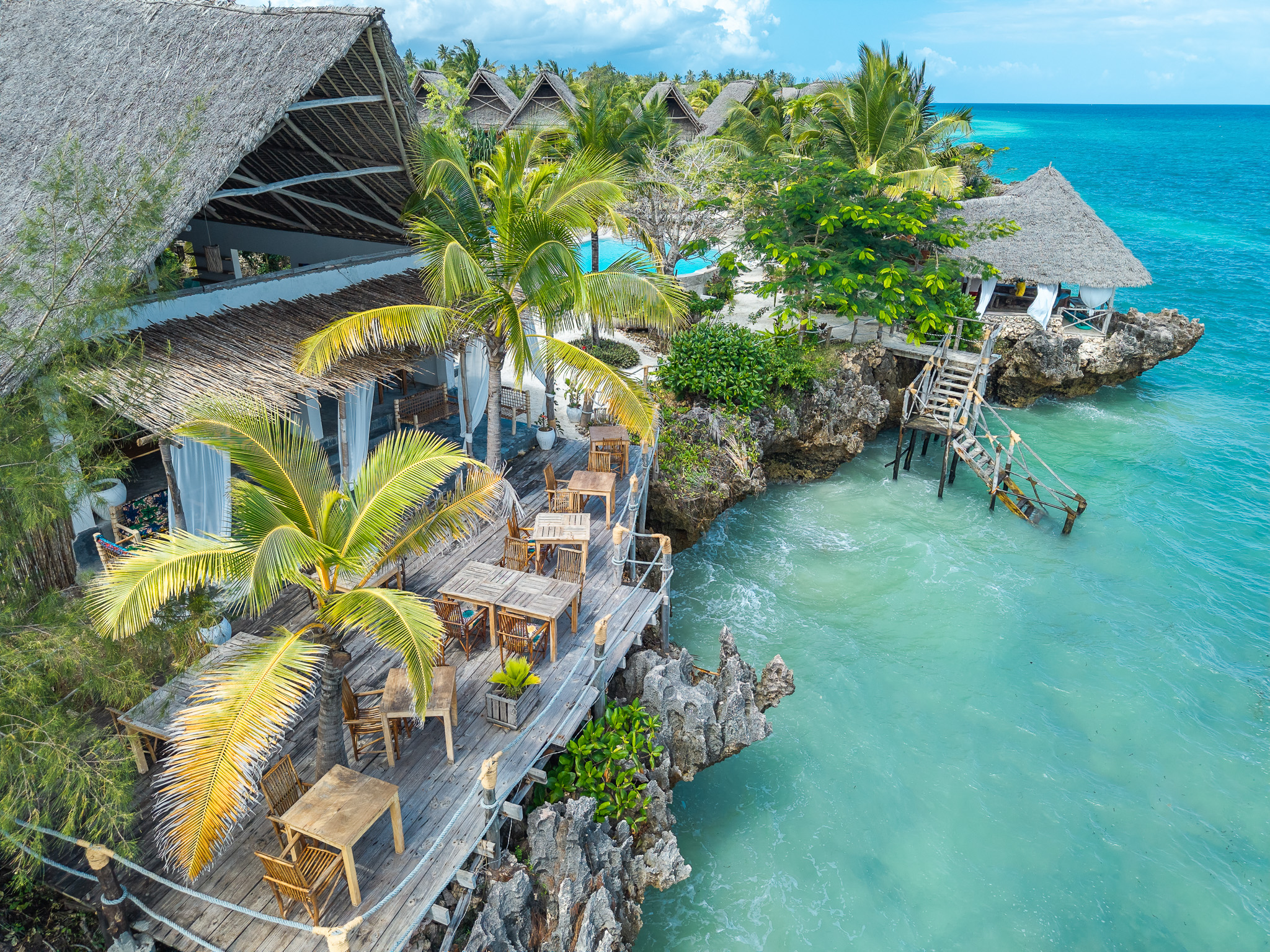 Aerial drone view of wooden overwater bungalows on rocky cliffs in Zanzibar