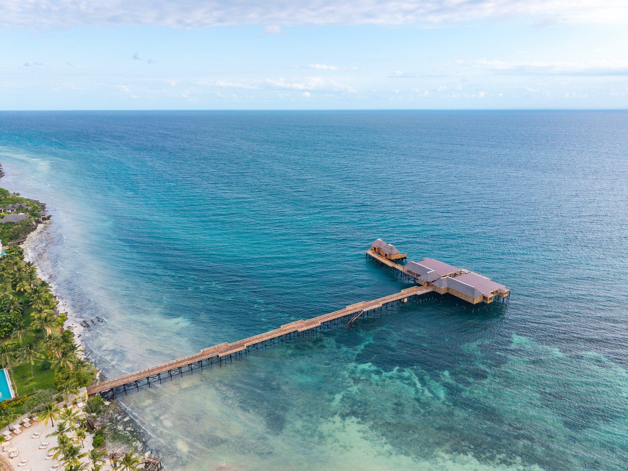 Aerial drone view of long wooden pier extending into turquoise Zanzibar ocean β hotel photography