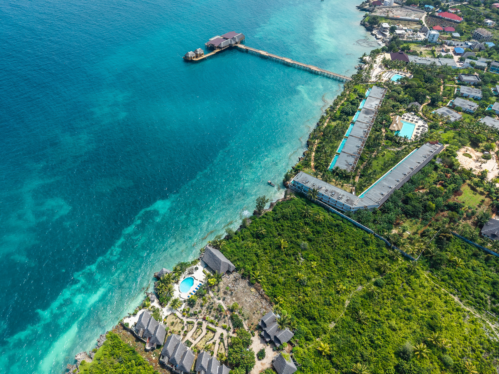Aerial drone view of Zanzibar hotel complex β pools, pier and turquoise ocean
