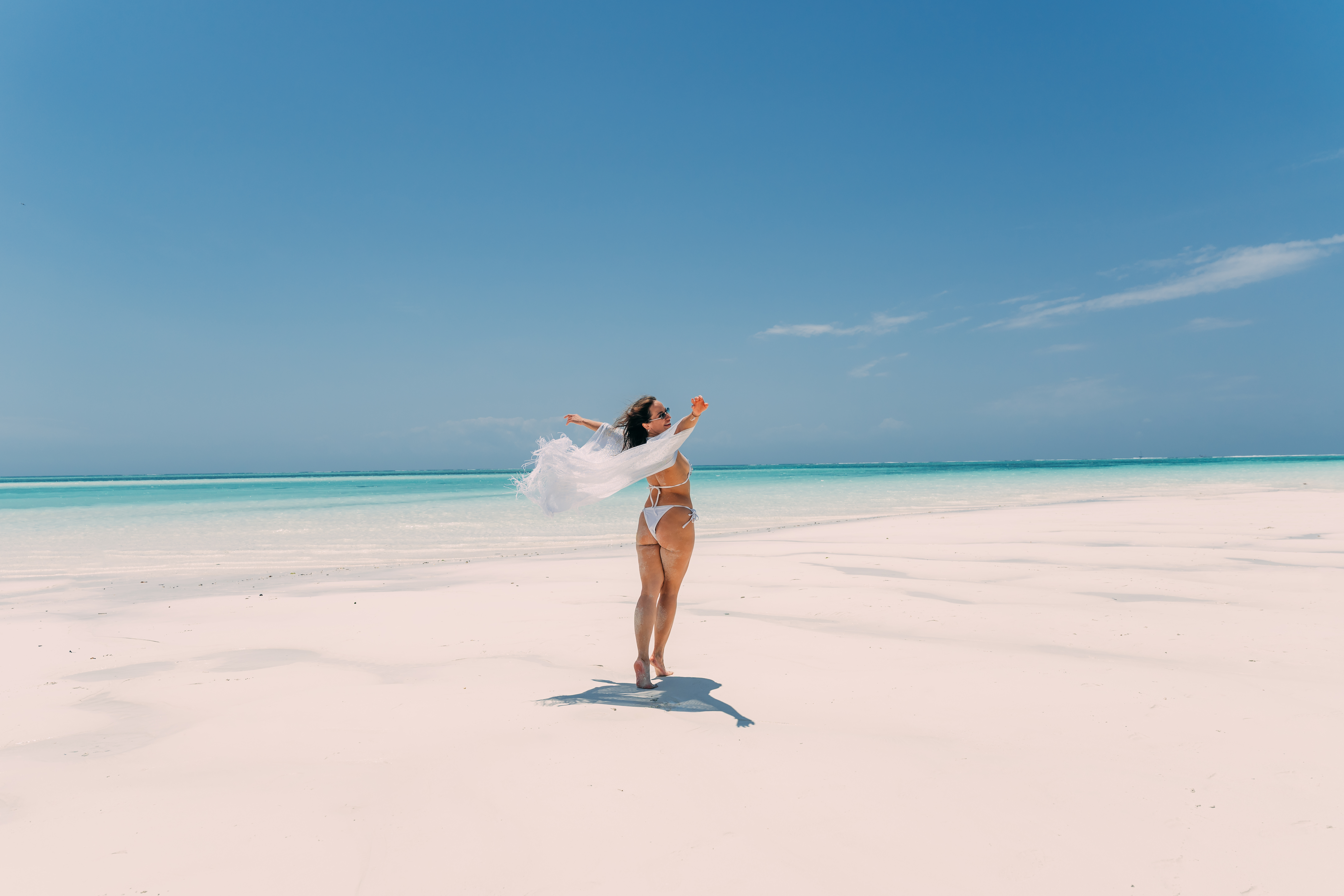 Woman in white outfit standing in turquoise ocean water at Nungwi secret beach Zanzibar